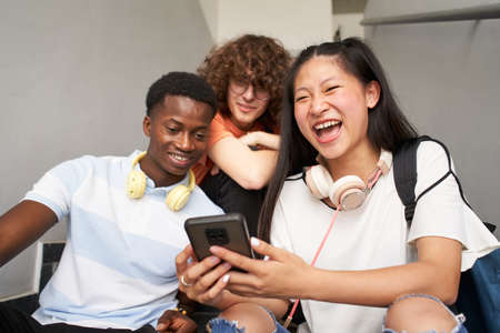 Group of adolescent students of different ethnicities using cell phones. Chinese girl looking at camera while laughing.の写真素材