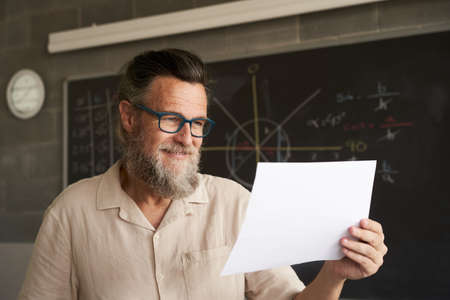 Close-up of the face of a smiling college professor. He is holding some documents, an exam, a paper.の写真素材