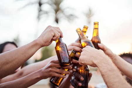 Close up of the hands of a group of friends cheering with beer outside. Concept of summer, friends, sunset, celebration,の写真素材