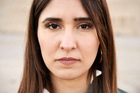 Close-up of a young woman with dark eyes looking at camera with serious expression on her face.の写真素材