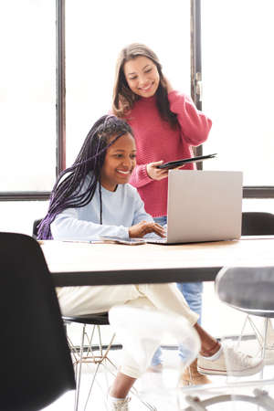 Vertical photo. In the office: two women work together. They discuss work issues amicably while looking at the computer screen.の写真素材
