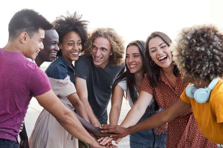 Friends of different ethnicities stacking hand and looking at each other. Group of people having fun and celebrating. Concept of friendship, happiness, joy.の写真素材