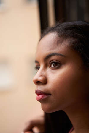 Vertical photo of an African-American girl leaning out the window. Dark cinematic shot.の写真素材