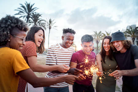 Group of friends smiling and having a good time around some sparklers. Mixed race youngsters enjoy spending time together in summer. Concept of friendship, free time, integration.の写真素材