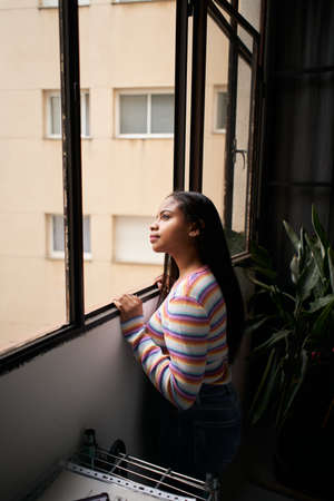Vertical photo. African American girl near the window. From home looking outside with a smile.