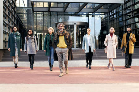 A multi-ethnic group of cheerful business people walking towards the camera outside a corporate...