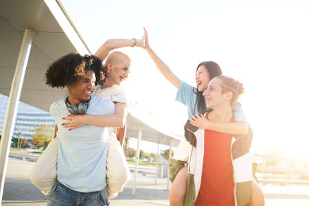 Centennials happy friends having piggyback and stacking hands on city street. Young people group together outdoors. Enjoying vacations, friendship and happy lifestyle conceptの写真素材