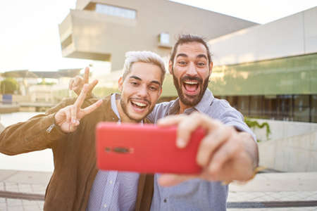 Happy gay couple taking smiling selfie with smartphone. Homosexual people having fun together.の写真素材
