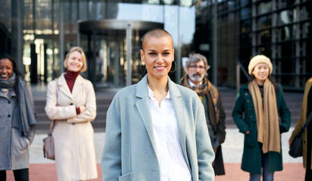 Empowered woman leads a team. Group of smiling business people outdoor in a corporate building.
