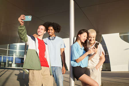 Happy centennial people using phones and taking smiling selfie. Group of students together at campus...