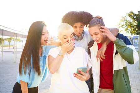 Friends amazed watching the smart phone outdoor. Young smiling people sharing with mobile cell outdoors.の写真素材