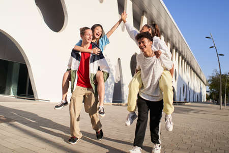 Centennials friends on vacation having piggyback and stacking hands on city street - Young people group enjoying time together laughing outdoors.の写真素材