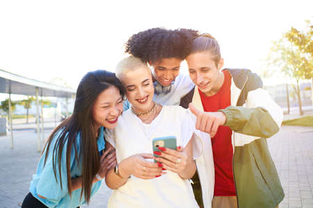 Group of happy friends using phone and having fun in the street. Teenagers sharing with mobile cell in video callの写真素材