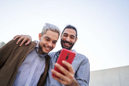 Homosexual man couple together using phones. Happy gay people watching something at mobile cell.