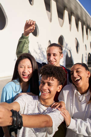 Vertical photo of a Latin guy taking a selfie with a multiracial group of people. Happy students together on campus college.の写真素材