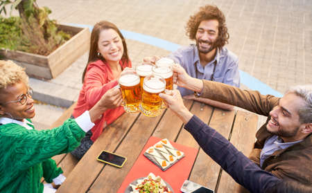 Happy multi ethnic friends drinking beer at terrace outdoors. The focus is on beers.の写真素材