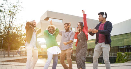 Group of happy people outdoors celebrating and dancing with headphones outdoors.の写真素材