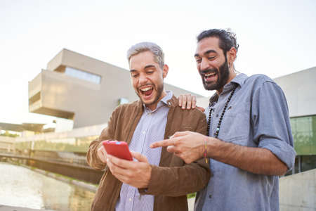 Portrait of a surprised gay couple watching something in their cell phone.の写真素材