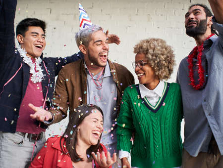 Young people blowing confetti from hands. Friends celebrating birthday outdoors.