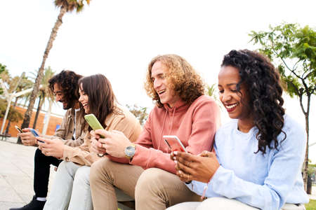 Friends having fun sharing in social media. Smiling mixed race group of friends sitting together on...