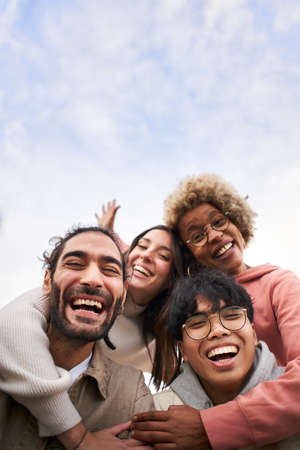Vertical pic of Group of young people looking at the camera outdoors. Happy smiling friends hugging. Concept of community and youth lifestyleの写真素材