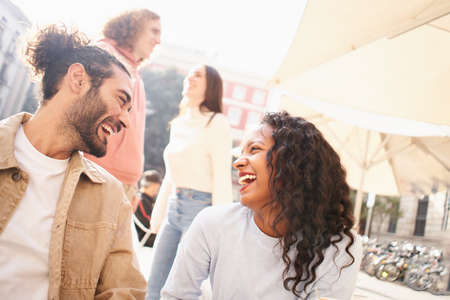 Heterosexual couples flirting outdoors on the terrace of a bar. Multiracial group of guys and girls...