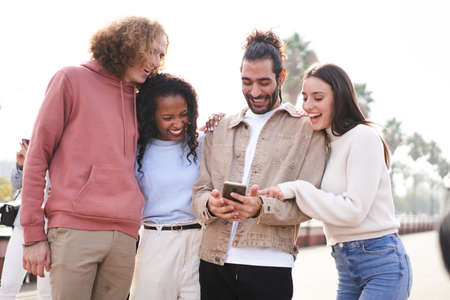 Group of happy friends using phone outdoors while walking al laughing.