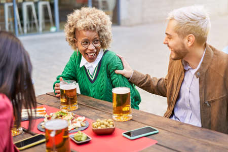 Multiracial couple having fun. Happy people celebrating drinking beer together with friends at...