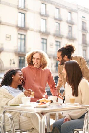Vertical photo of Friends group toasting latte at coffee bar terrace. Group of people talking and having fun together at cappuccino restaurant. Lifestyle concept with happy men and womenの写真素材