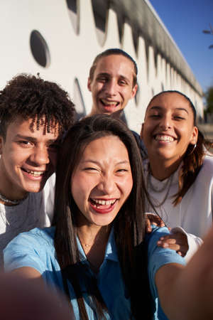 Vertical photo of a Chinese girl taking a selfie with a multiracial group of people. Happy students together on campus college.の写真素材