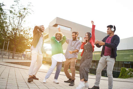Group of co-workers celebrating.Cheerful People Dancing outdoors at sunset. Young Millennials with headphones listening music.の写真素材