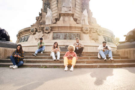 Addicted group of friends using their smart phones. Individualistic people focused on their mobiles sitting on a staircase in a city. Technology and individualism concept.の写真素材