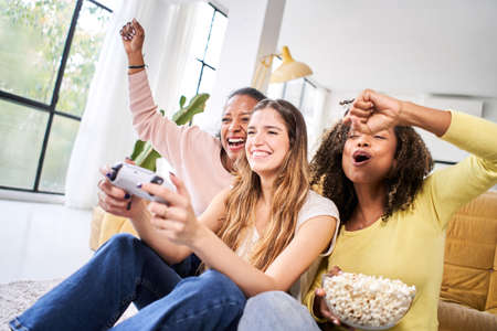 Only women gaming. Three young female multiracial young friends play video games together at home - Celebrate victory win.の写真素材