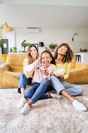 Vertical photo Group of young female multiracial young friends play video games together at home. Only women gaming and eating popcorns.の写真素材