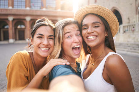 Three funny beautiful girls friends in summer clothes taking a selfie outdoors at the touristic urban center cityの写真素材