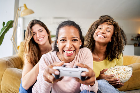 Young friends play video games together at home. Only women gamers celebrating and eating popcorns.の写真素材
