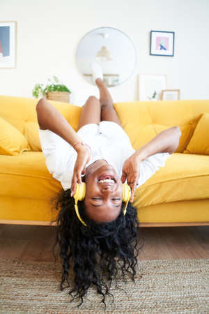 Vertical photo of motivated young woman listening to music with headphones sitting on sofa at home.の写真素材
