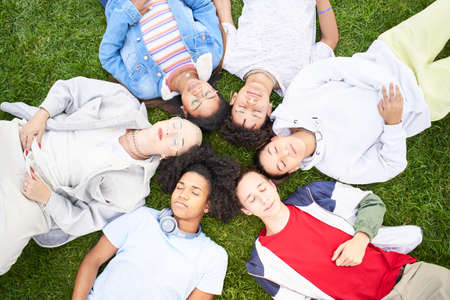 Boys and girls lying on grass with eyes closed. They are tranquil and satisfied. Top view portrait