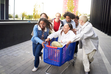 Crazy friends making a racing challenge with shopping cart. Multiracial group of young people having fun outsideの写真素材