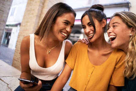 Portrait of pretty charming multiracial women laugh reading news or sms using phones outdoors.の写真素材