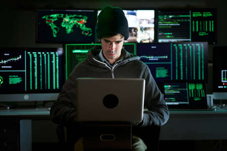 Front Shot from to Hacker Breaking into Corporate Data Servers from His Underground Hideout. Place has dark atmosphere, multiple displaysの写真素材
