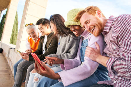 Group of multirracial friends using mobile cell together outdoors having fun watching smart phone. Diversity People Meeting Relaxing Connection Communication Community Concept.の写真素材