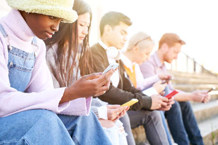 Group of multirracial friends using mobile cell together outdoors watching smart phone with serious face. Diversity People Meeting Relaxing Connection Communication Community Concept.の写真素材