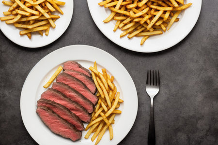Slices of steak with french fries on dark background. top viewの素材