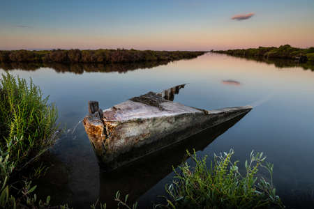 Abandoned boat on the shore of a marsh at duskの写真素材