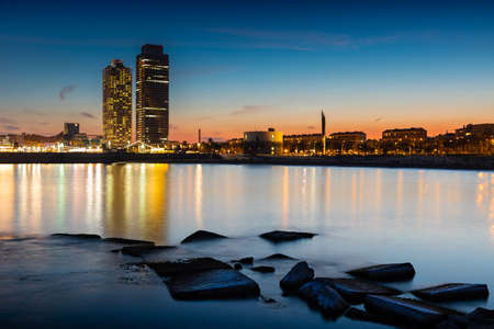 Dusk on the coast of Barcelona. Emblematic image of the Barcelona coastline illuminated at dusk with the calm sea and reflections of lightsの写真素材