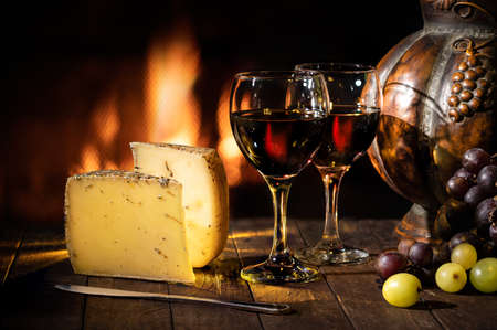 Wine cellar with wine glasses, cheese, grapes on rustic wooden table with fireplace in the backgroundの写真素材