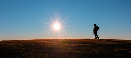 Silhouette of a lone hiker with backpack and trekking pole against the radiant sunsetの写真素材