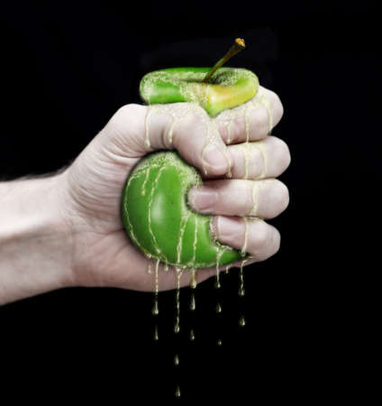 hand to squeeze a green apple isolated in black backgroundの写真素材