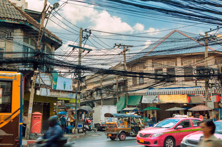 Lifestyle and street environment in Bangkok, Thailand. Traffic tuk tuk, pink taxis and traditional buses. Tangle of electric cables and house facadesの写真素材